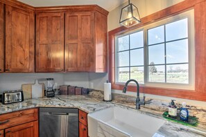 A kitchen with wooden cabinets, a built-in dishwasher, a large window with a view, and a marble countertop. - Secluded Bonanza Home w/ Antique Furnishings (Bonanza)