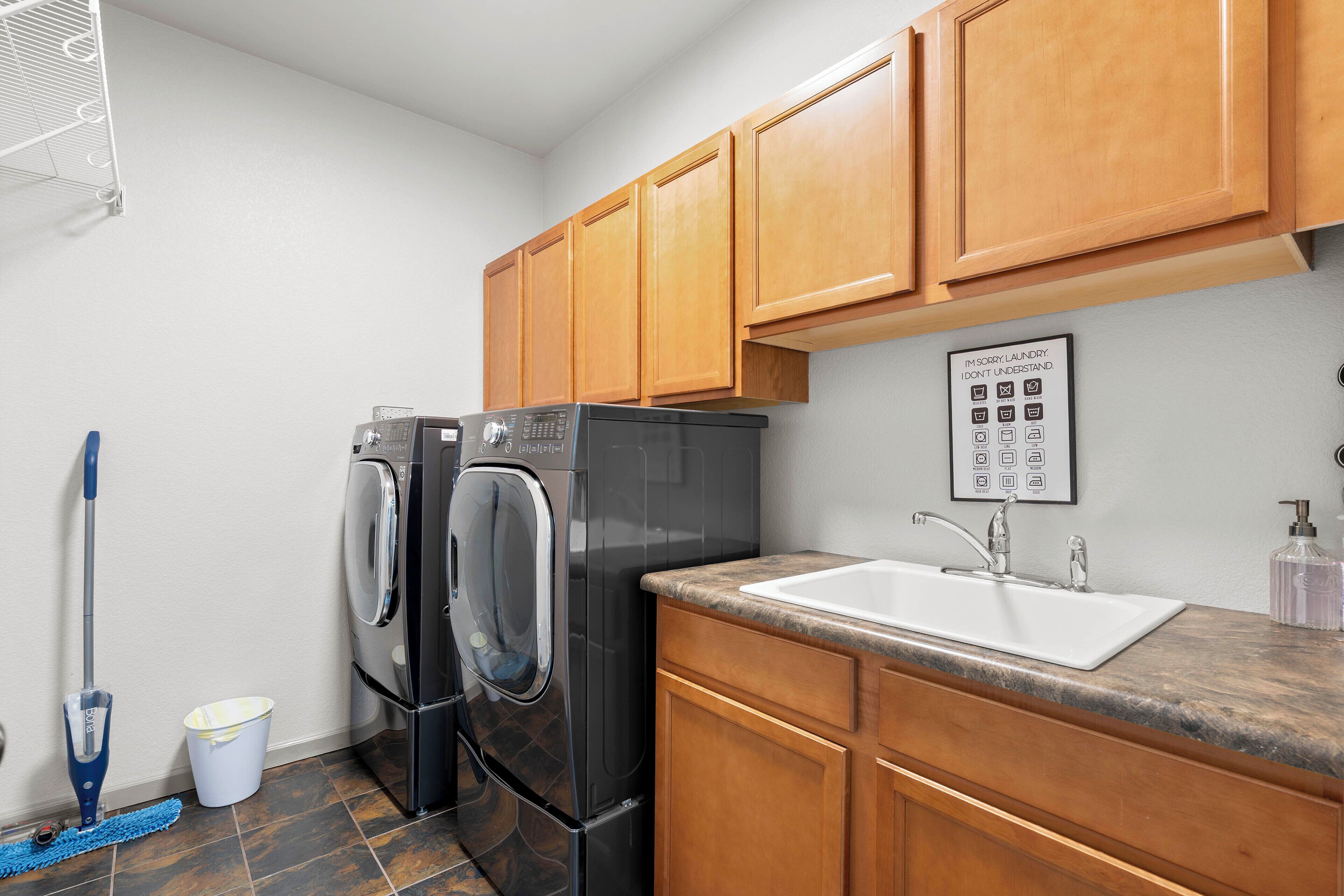 A compact kitchen with wooden cabinets, a built-in washer and dryer, a sink, and a mop.