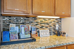 A kitchen counter with a tiled backsplash, wooden cabinets, and a display of travel guides. - Mountain-view Deck! Pueblo Family Home (Pueblo)