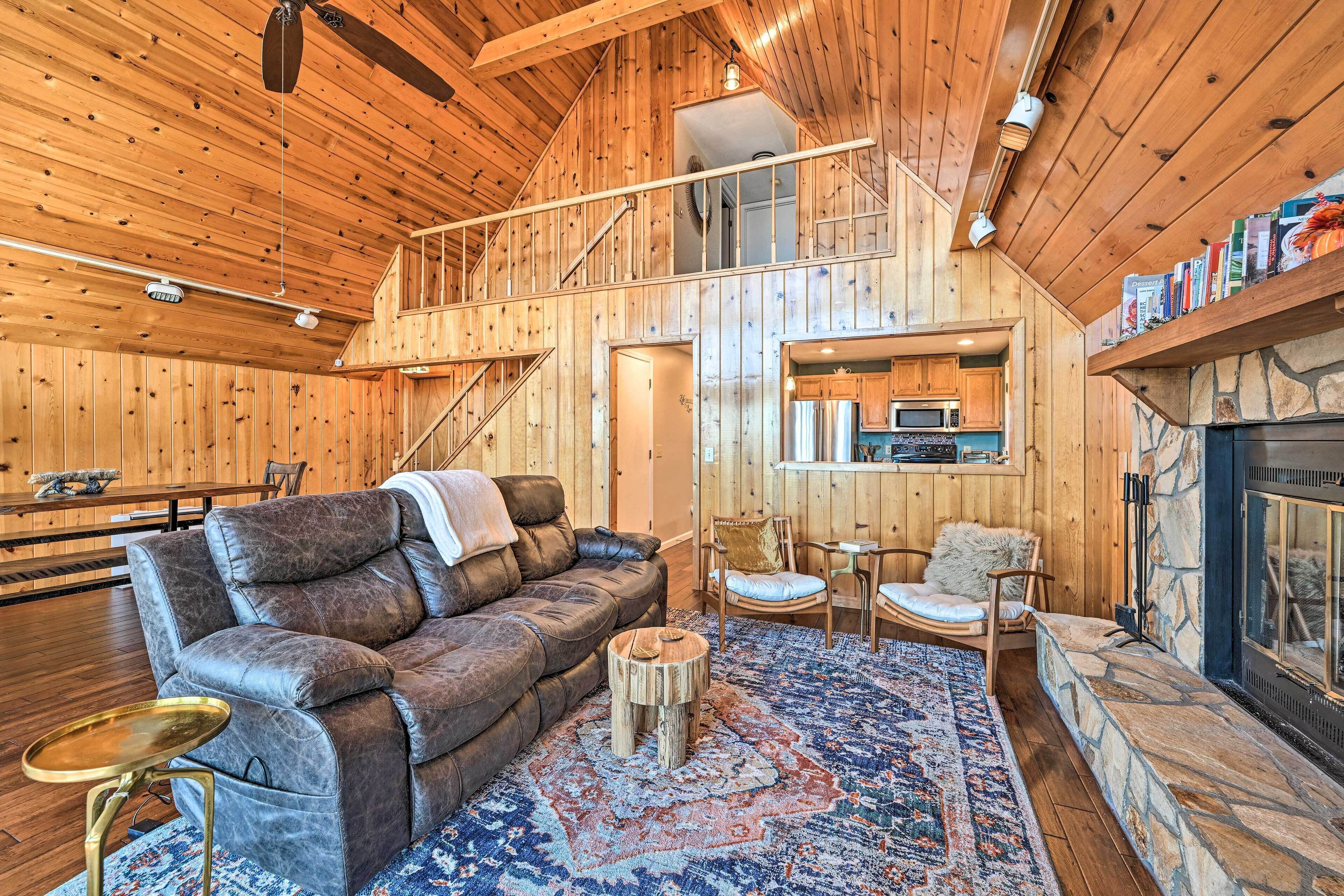 A cozy cabin interior with a leather sofa, a dining table, a fireplace, and a kitchen area.