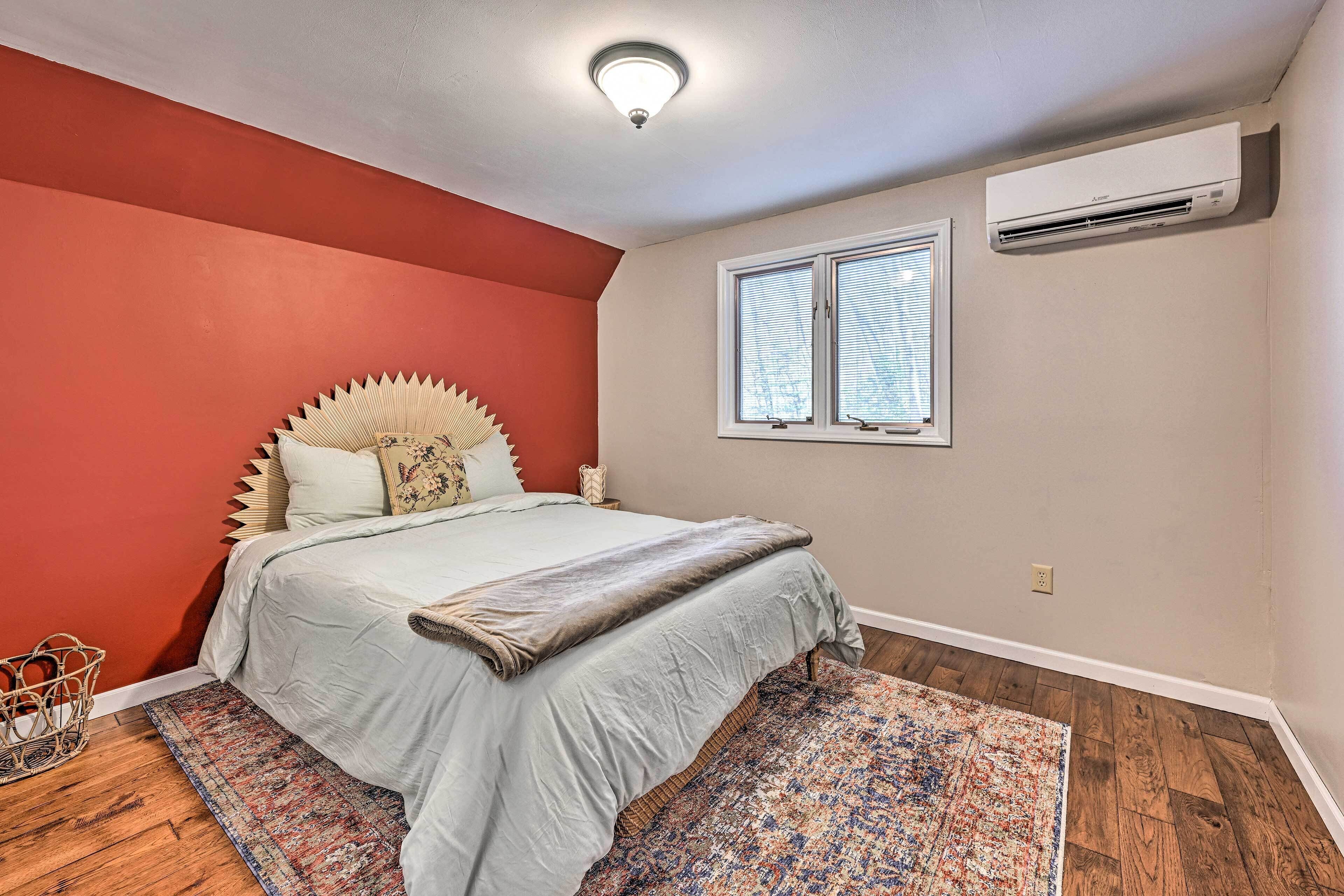 Ein Schlafzimmer mit Bett, Fenster, Klimaanlage und einer roten Wand.