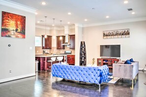 A modern living room with a blue sofa, a television, and a kitchen in the background. - Pet-friendly Houston Townhome, 6 Mi to Dtwn! (Houston)