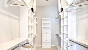 Un petit dressing étroit avec des étagères et des tiroirs blancs, doté de supports à vêtements en métal et d'une armoire blanche centrale.