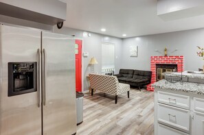 Eine moderne Küche mit einem Edelstahlkühlschrank, einer integrierten Kaffeemaschine, einer roten Tür, einem gemusterten Sessel, einer schwarzen Couch, einem Kamin und einer Arbeitsplatte aus Granit.