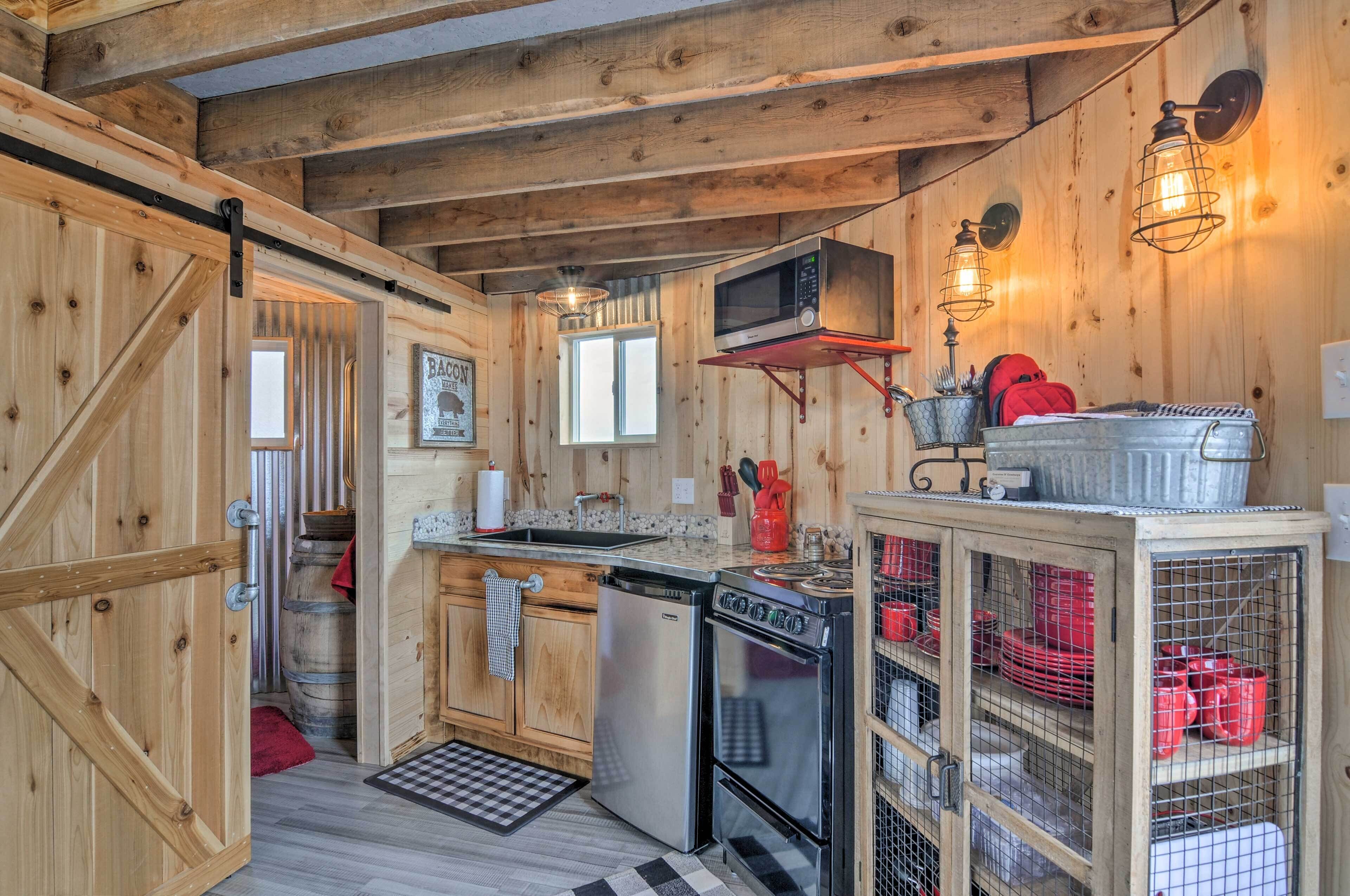 A rustic kitchen with wooden walls, a built-in microwave, a stove, and a cabinet with red dishes.