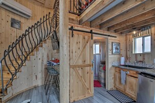 A rustic interior with a wooden staircase, a kitchen area with a sink and cabinets, and a dining space with stools.