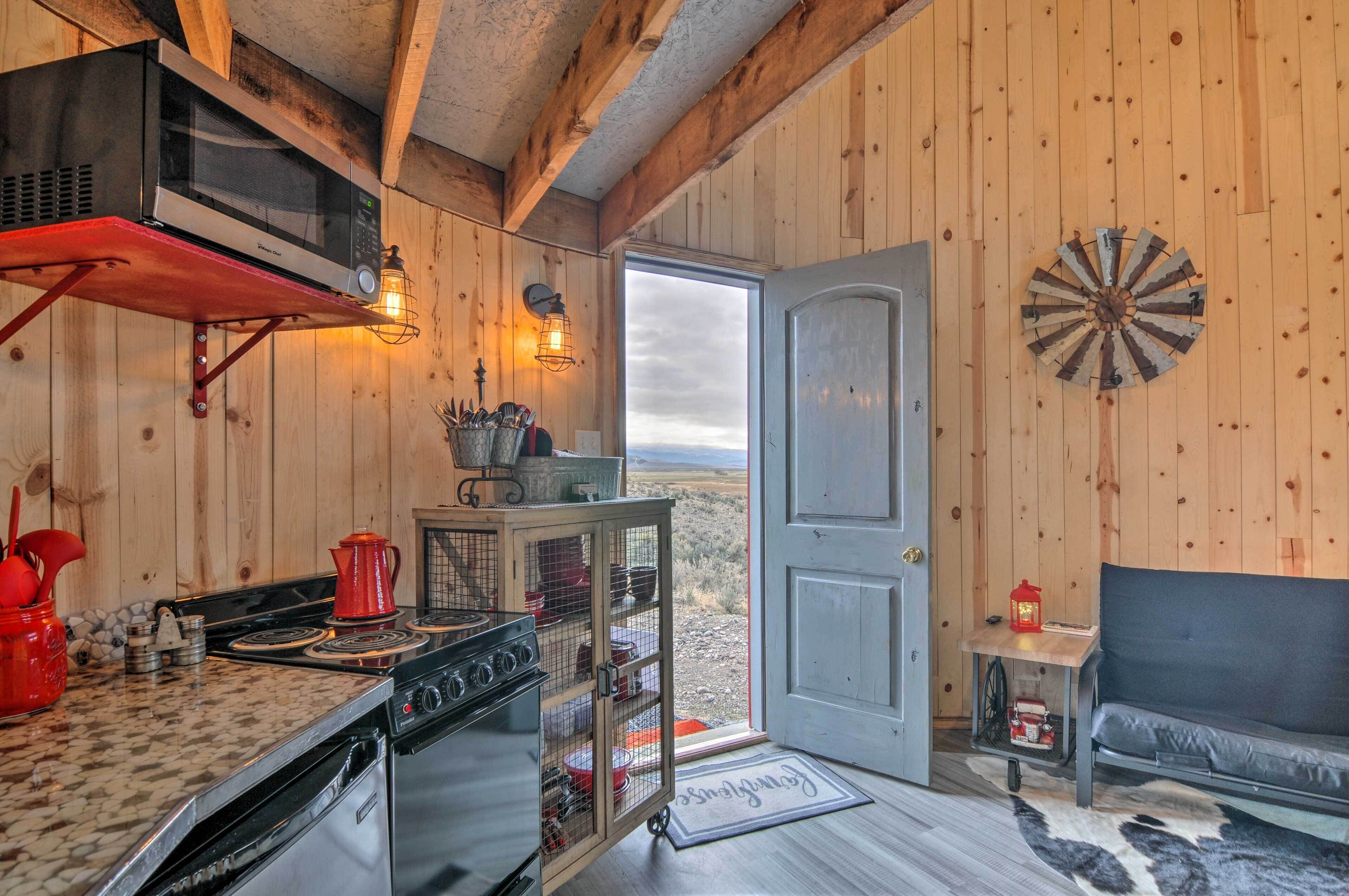 Een rustiek houten huisje van binnen, met keuken, eethoek en een deur naar een prachtig uitzicht.