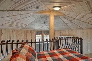 A rustic room with wooden walls and ceiling, a metal bed frame, and a checkered bedspread.
