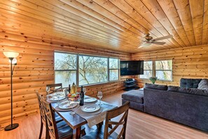L’intérieur d’un chalet en bois comprend une table à manger dressée pour quatre personnes, un canapé et un téléviseur.