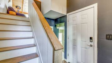 A staircase with wooden steps and a handrail, leading to a door with a light switch and a keypad lock.