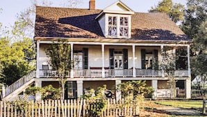 A two-story house with a porch, a staircase, and a fenced yard. - Vintage Louisiana Vacation Rental Home (New Roads)