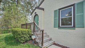 Una casa con puerta verde, escalera de madera y ventana con contraventanas verdes.