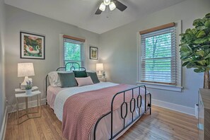 A bedroom with a bed, two bedside tables with lamps, a ceiling fan, and large windows with blinds. - Benton Harbor 'gracie Cottage' w/ Hot Tub + Yard! (Benton Harbor)