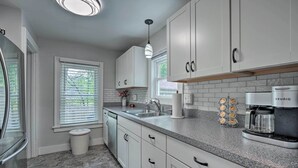 Una cocina moderna con armarios blancos, encimeras de granito, lavavajillas integrado y una cafetera Keurig.