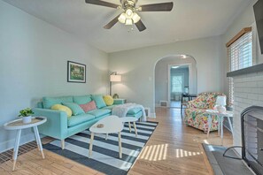 A living room with a teal sofa, a floral armchair, a fireplace, and a ceiling fan. - Benton Harbor 'gracie Cottage' w/ Hot Tub + Yard! (Benton Harbor)