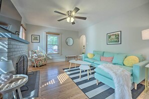 A living room with a teal sofa, a fireplace, a ceiling fan, and a striped rug. - Benton Harbor 'gracie Cottage' w/ Hot Tub + Yard! (Benton Harbor)
