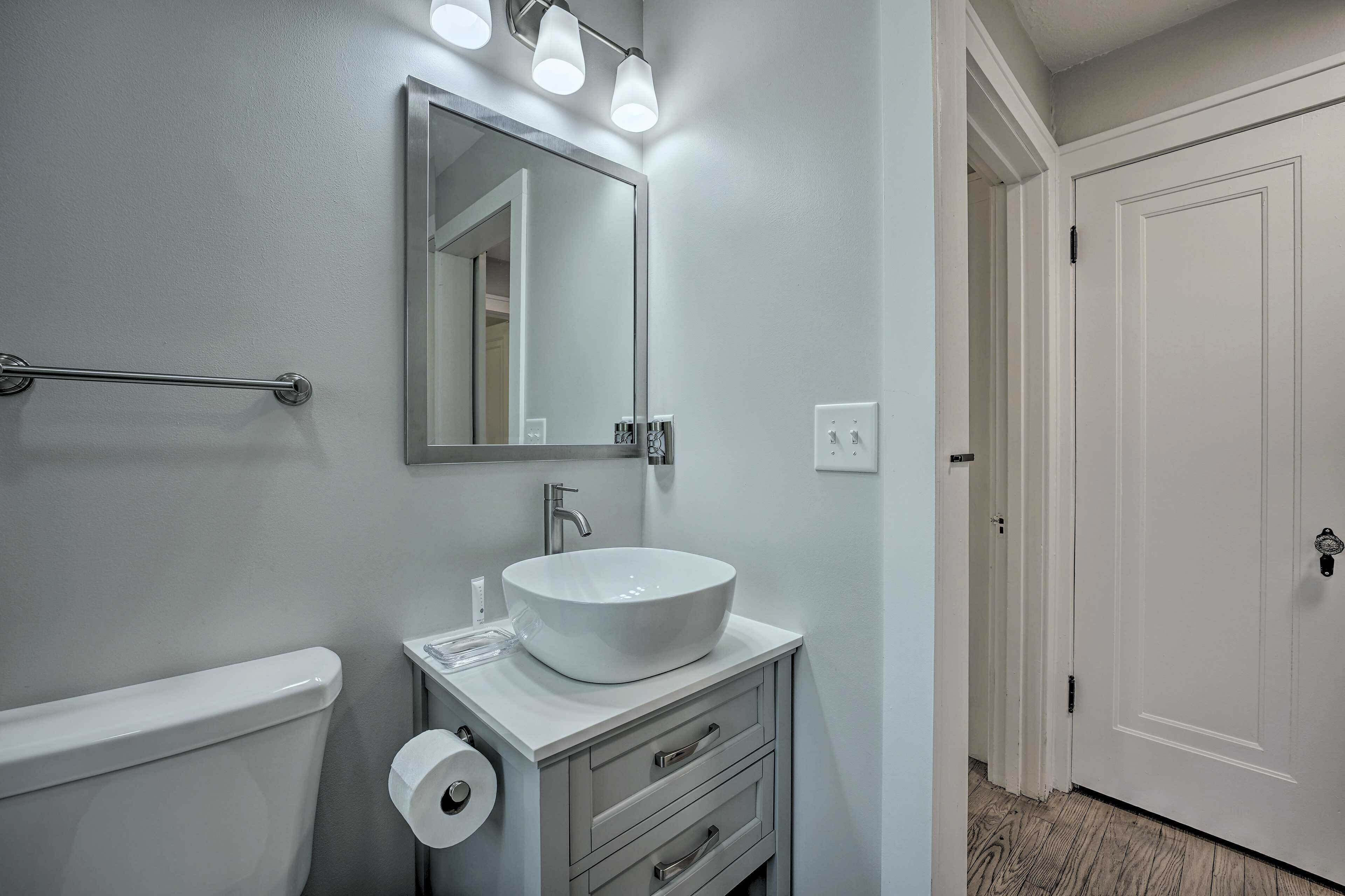 A bathroom with a white sink, a mirror, and a toilet. There is a towel rack above the sink and a door to the right.