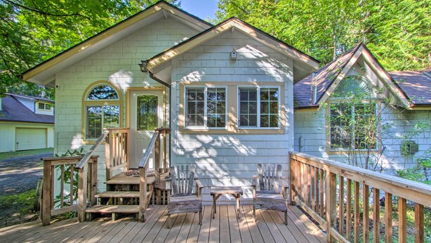 Ein helles Holzhaus mit Veranda, zwei Stühle, einem kleinen Tisch und einem Hollerker.