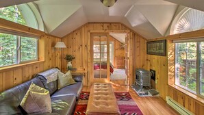 Ein gemütliches Blockhausschlafzimmer mit Holzvertäfelung, einer Ledersofa, einer Bank, einem Kamin und großen Fenstern mit Blick auf den umliegenden Wald.