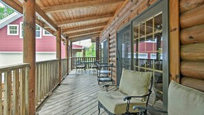A wooden porch with a covered seating area, a railing, and a view of a red building in the background.