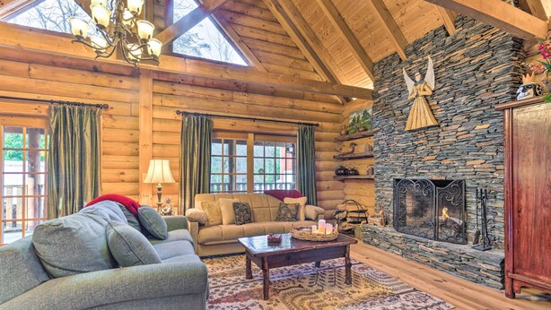 A log cabin interior with a stone fireplace, wooden ceiling beams, and a cozy living area with a sofa and coffee table.