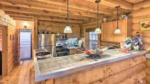 A rustic wooden cabin kitchen with a stone countertop, wooden cabinets, and hanging pendant lights.