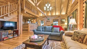 A log cabin interior with a wooden staircase, a television, a sofa, and a coffee table.