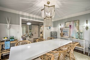 A dining area with a white table, wicker chairs, a chandelier, and a buffet table with bottles. - Stunning Charlotte Home: Private Pool! (Charlotte)