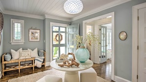 A room with a white bench, a round table with a vase and decorative items, and a large window with a wreath. - Stunning Charlotte Home: Private Pool! (Charlotte)