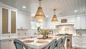 A spacious kitchen with white cabinetry, a large island, wicker chairs, and pendant lighting. - Stunning Charlotte Home: Private Pool! (Charlotte)