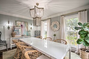 A dining area with a white table, wicker chairs, a chandelier, and a view of greenery outside. - Stunning Charlotte Home: Private Pool! (Charlotte)