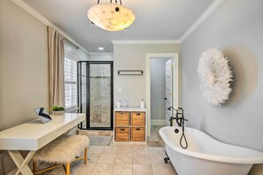 A modern bathroom with a white bathtub, a shower with a glass door, a white desk with a laptop, and wicker baskets. - Stunning Charlotte Home: Private Pool! (Charlotte)