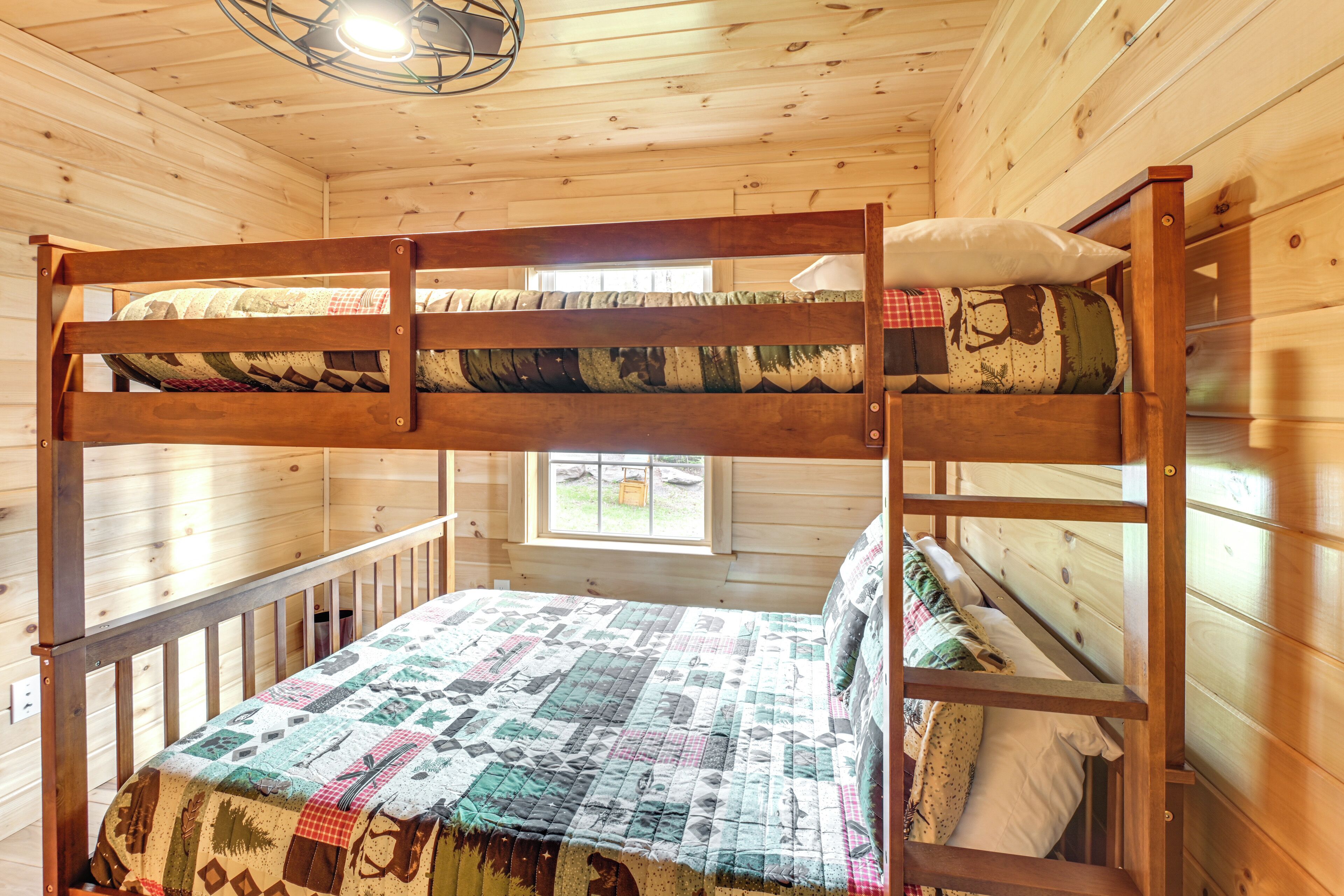 Una cama litera con colcha, paredes de madera y una ventana.