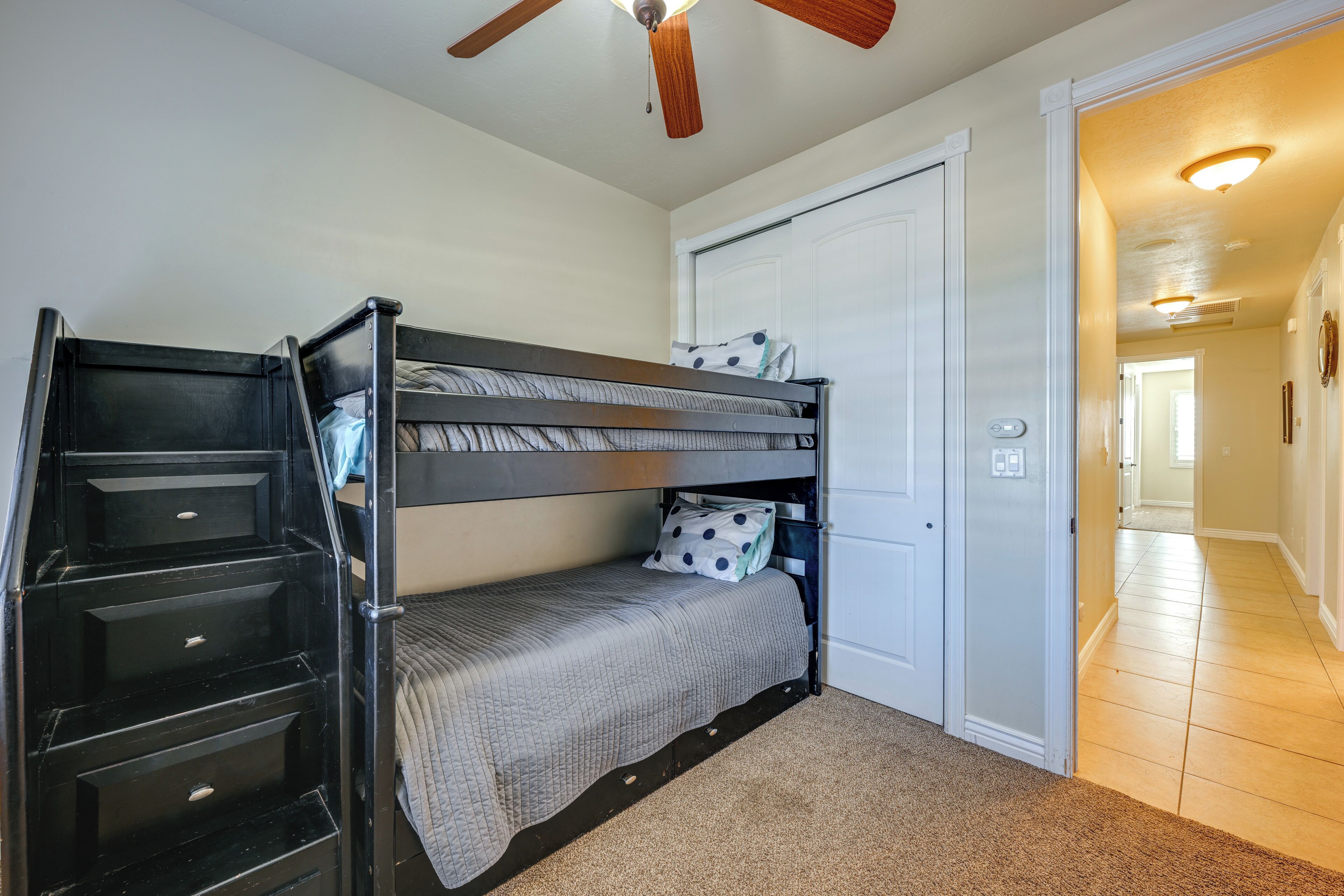 A bunk bed room with a ceiling fan, a white door, and a hallway leading to another room.