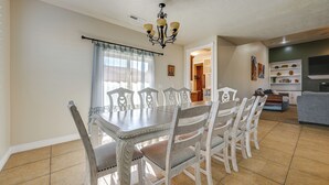 A dining area with a round table and six chairs, a chandelier, a window with curtains, and a kitchen area in the background. - Utah Retreat w/ Heated Pool, Grill & Fire Pit! (Hurricane)
