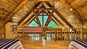 Un espacioso dormitorio en el ático con un alto techo de madera, un gran ventanal con vistas a árboles y una bandera colgada en la ventana.