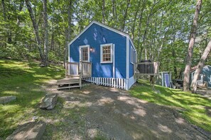 Une petite cabane bleue avec une terrasse en bois et un petit abri situé à proximité.