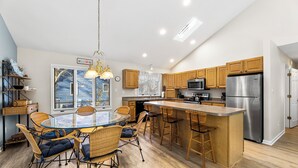 Una cocina moderna con una isla central, armarios de madera, electrodomésticos de acero inoxidable y un comedor con sillas de mimbre.