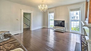 A spacious living room with hardwood floors, a chandelier, a TV, and a staircase leading to another level. - Historic Troy Home Enjoyable Dining Steps Away (Troy)