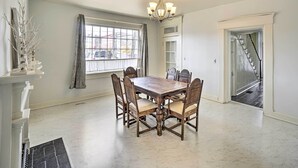 A dining room with a wooden table and chairs, a chandelier, a window with curtains, and a staircase leading to another room. - Historic Troy Home Enjoyable Dining Steps Away (Troy)