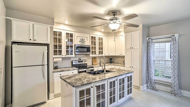 A kitchen with white cabinets, a built-in microwave, a refrigerator, a ceiling fan, and a window with curtains. - Historic Troy Home Enjoyable Dining Steps Away (Troy)