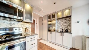 Une cuisine moderne dotée d’appareils électroménagers en acier inoxydable, de meubles blancs et d’un revêtement mural décoratif.