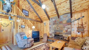 Interior acogedor de una cabaña de troncos con chimenea de piedra, televisor y un sofá mullido.