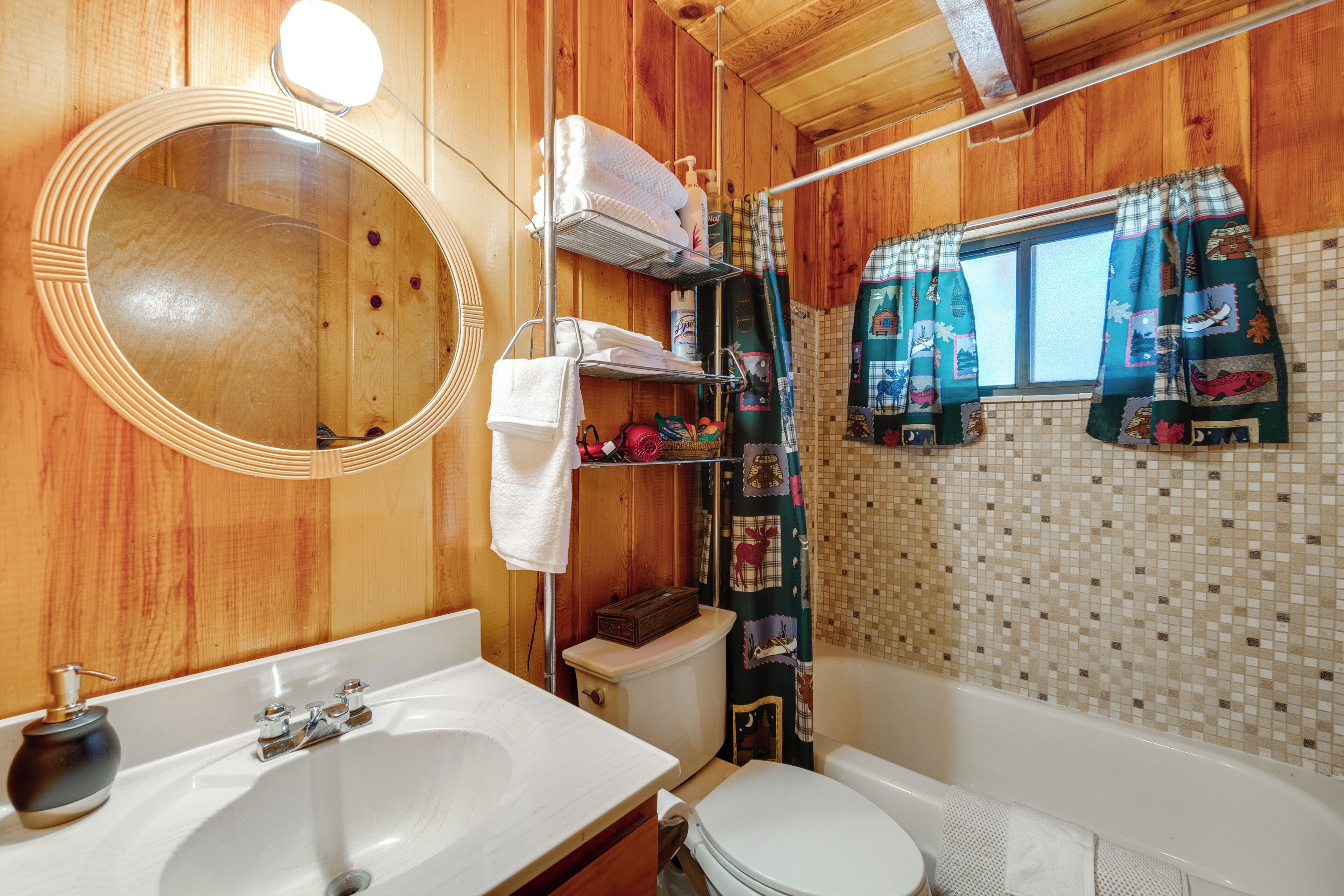 Ein Badezimmer mit Holzwandverkleidung, einem weißen Waschbecken, einem runden Spiegel, einer Toilette und einer Badewanne.