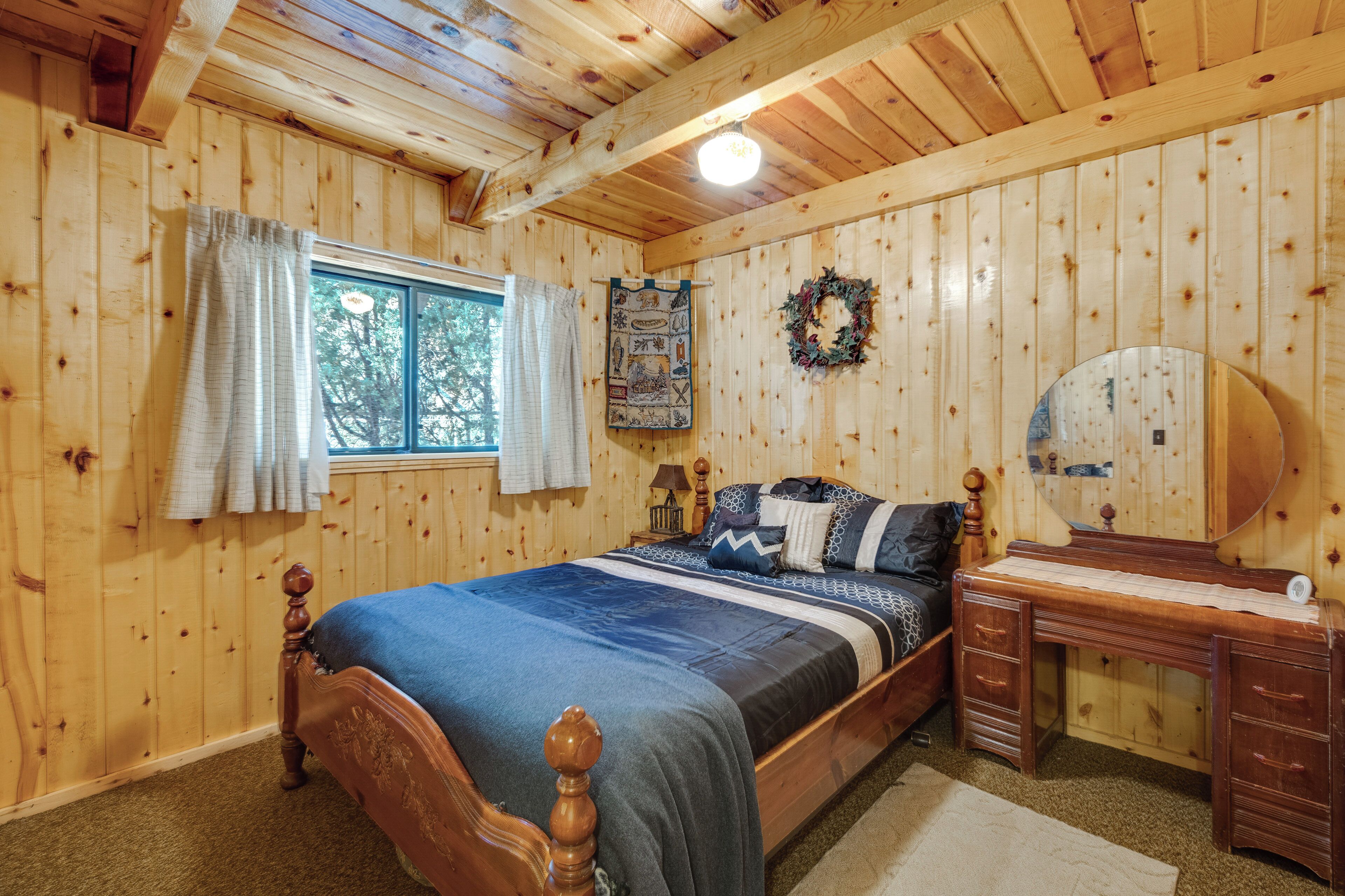 A wooden-paneled bedroom with a bed, a dresser, a mirror, a window with curtains, and a wall hanging.