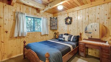 A wooden-paneled bedroom with a bed, a dresser, a mirror, a window with curtains, and a wall hanging.