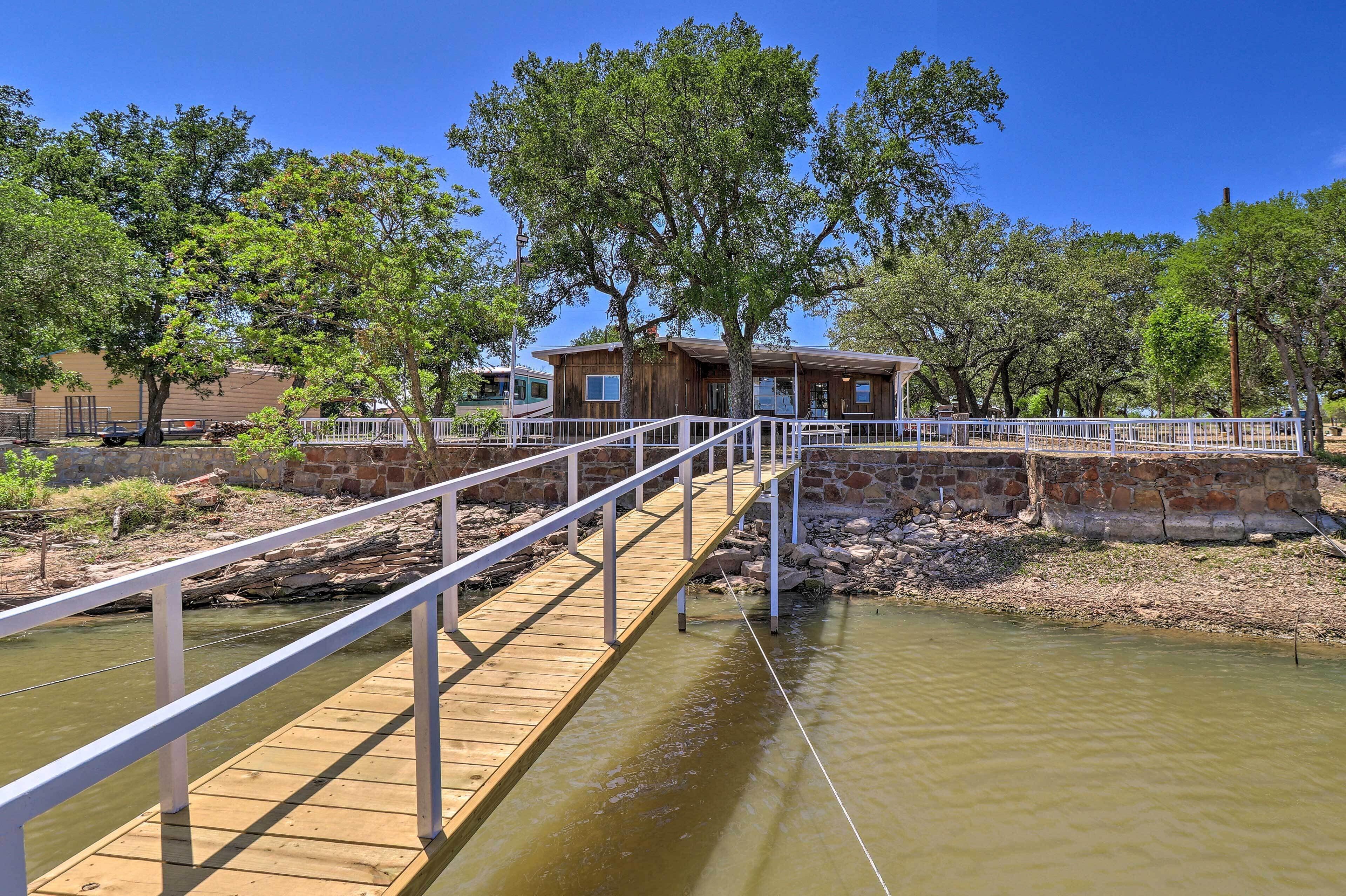 A wooden bridge over a calm river leading to a rustic building with a white railing.