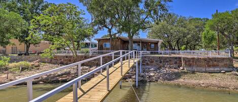 A wooden bridge over a calm river leading to a rustic building with a white railing.