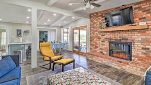 A spacious living room with a brick fireplace, a ceiling fan, and a television mounted on the wall. - Private Dock - Waterfront Lake Brownwood Gem! (Brownwood)