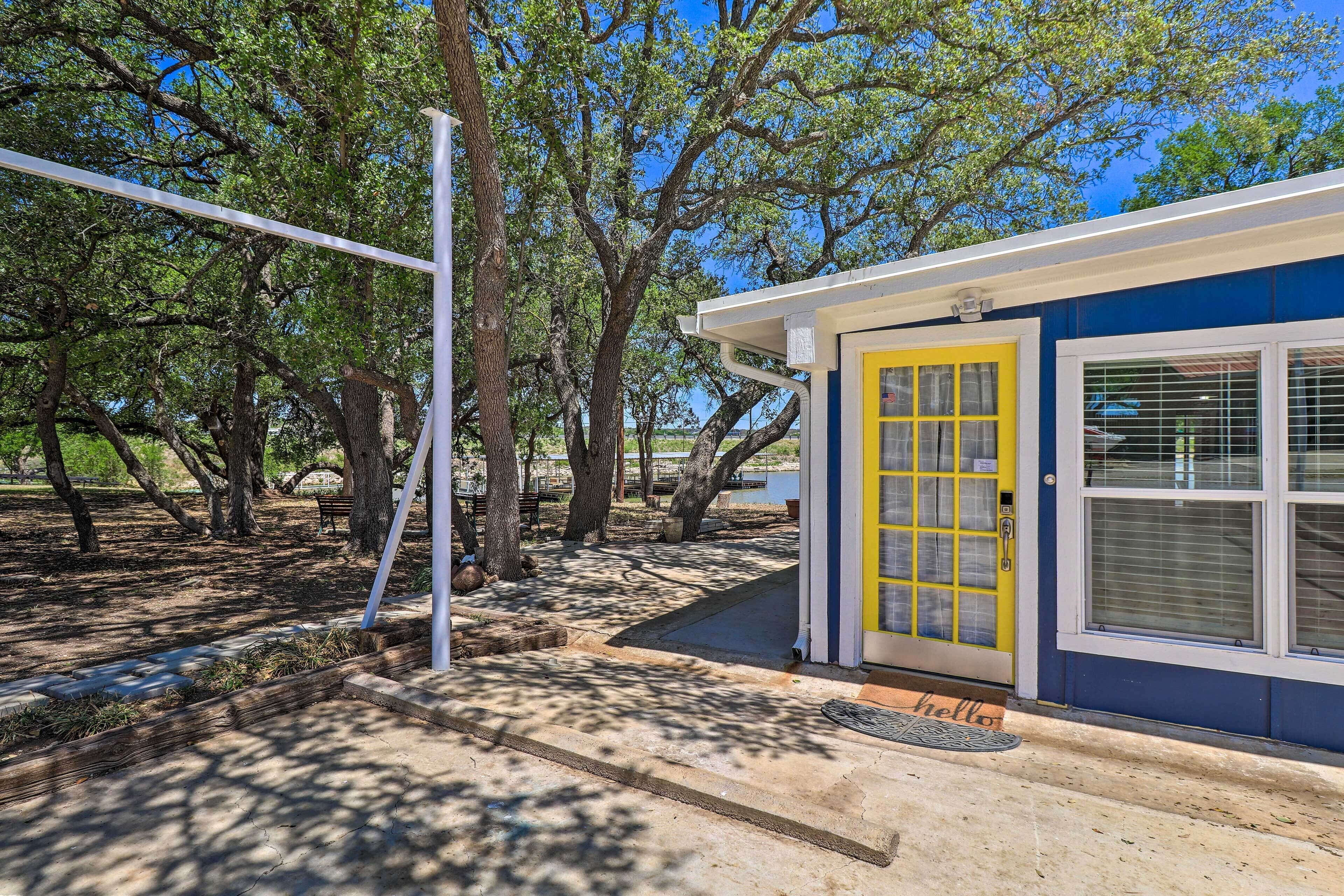 A small building with a yellow door and a window with blinds, surrounded by trees and a clear sky.